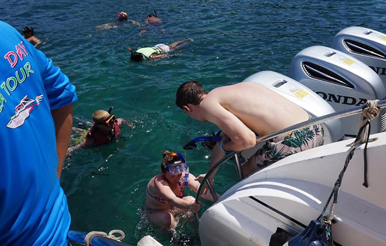 People jumping off and climbing back on the back of a boat